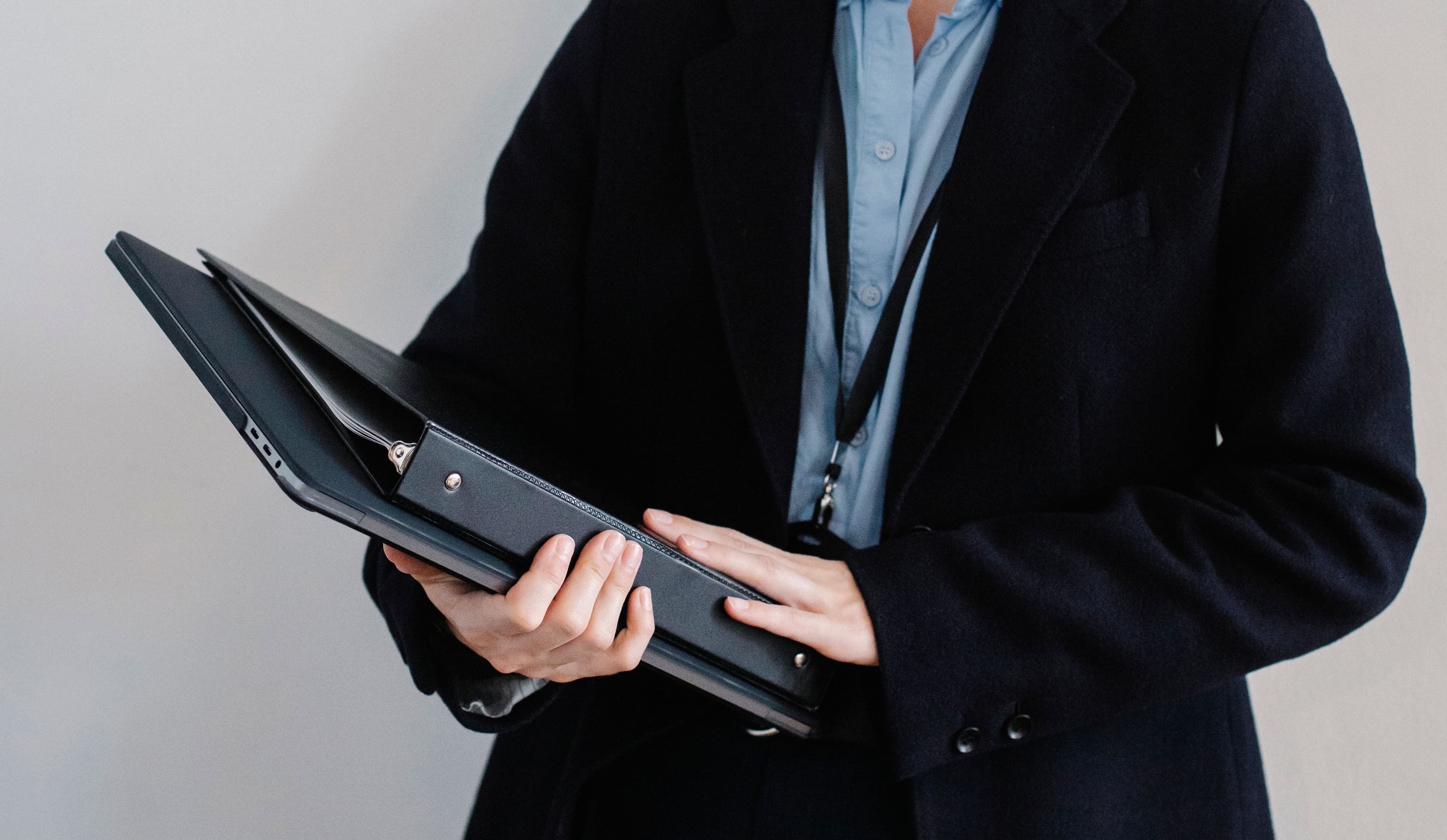 A person in a dark suit holding an open binder of company documents.