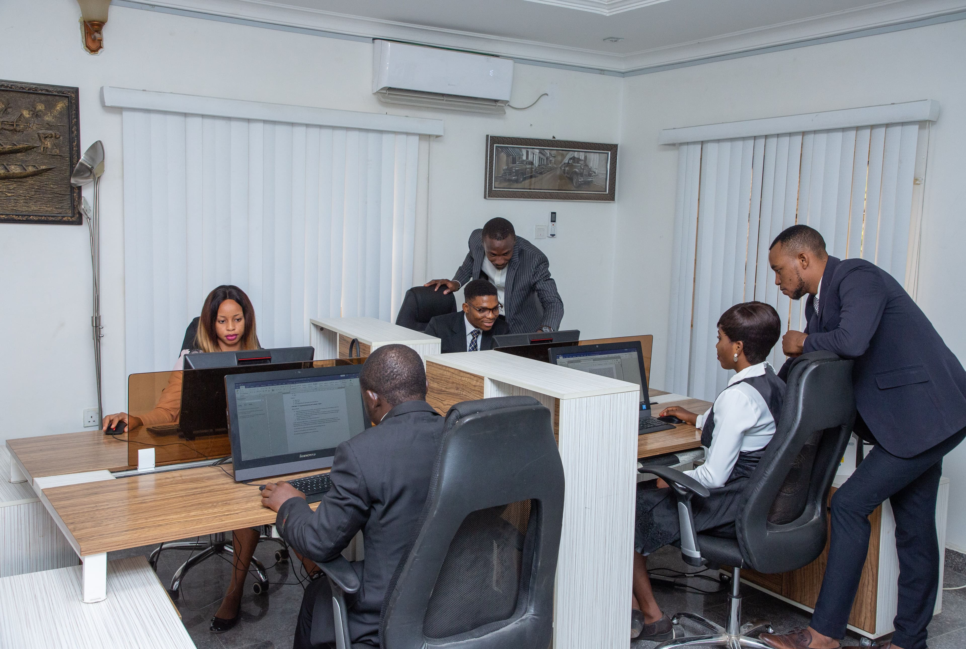 A team of five professionals working at computers in a small shared office.