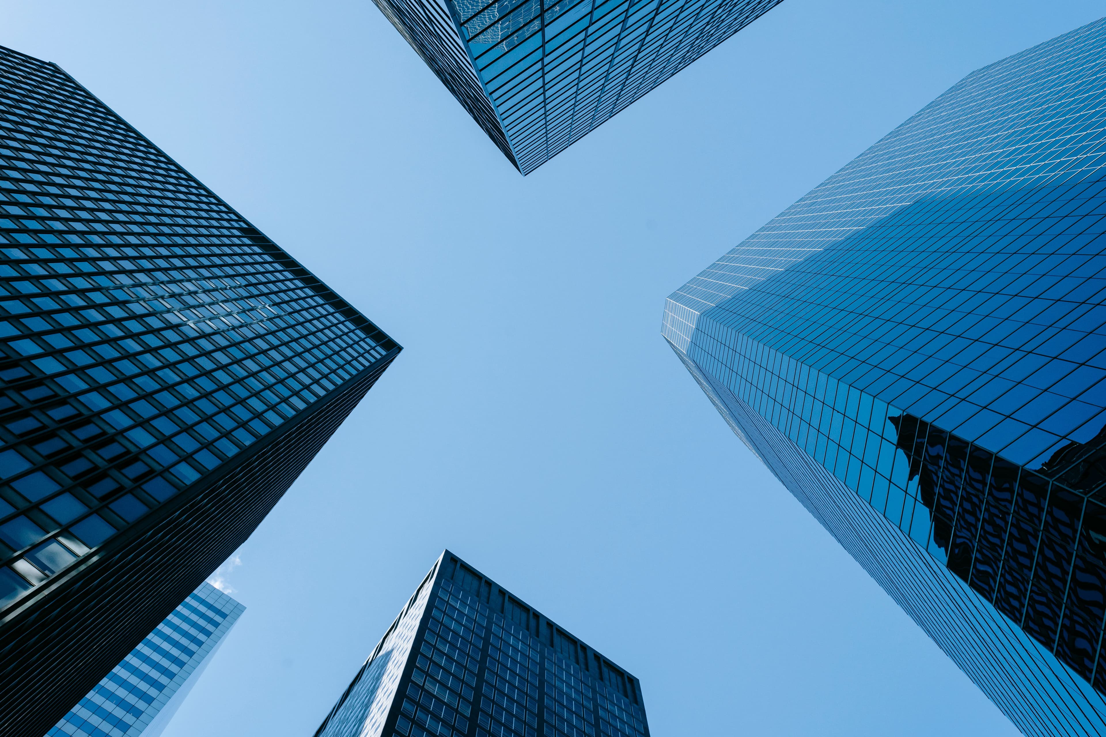 Looking straight up at glass-fronted office towers against a clear blue sky.