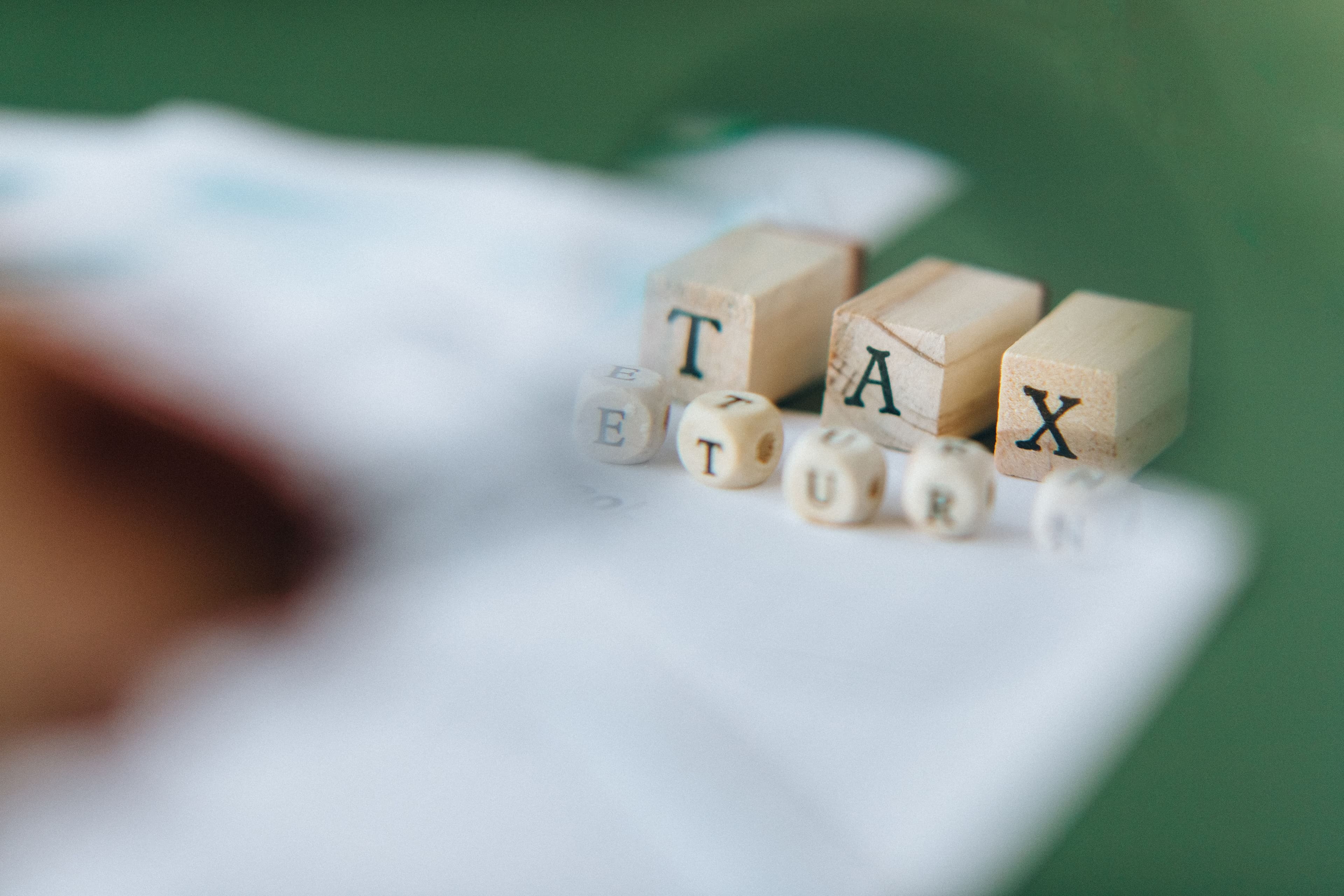 Wooden letter blocks spelling "Tax Return" resting on a pile of paperwork.