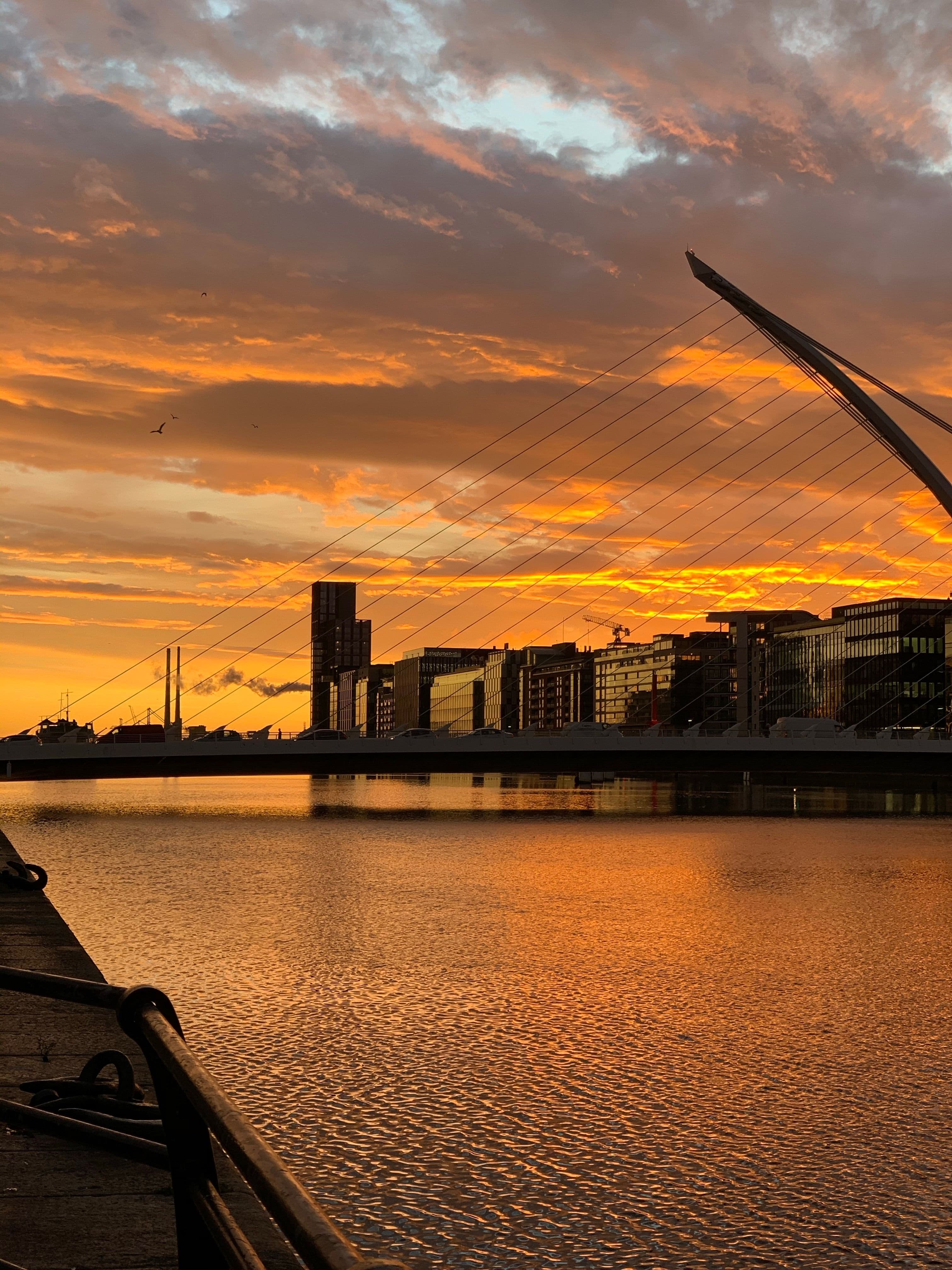 The Samuel Beckett Bridge over the River Liffey in Dublin at sunset, with office buildings along the quay.